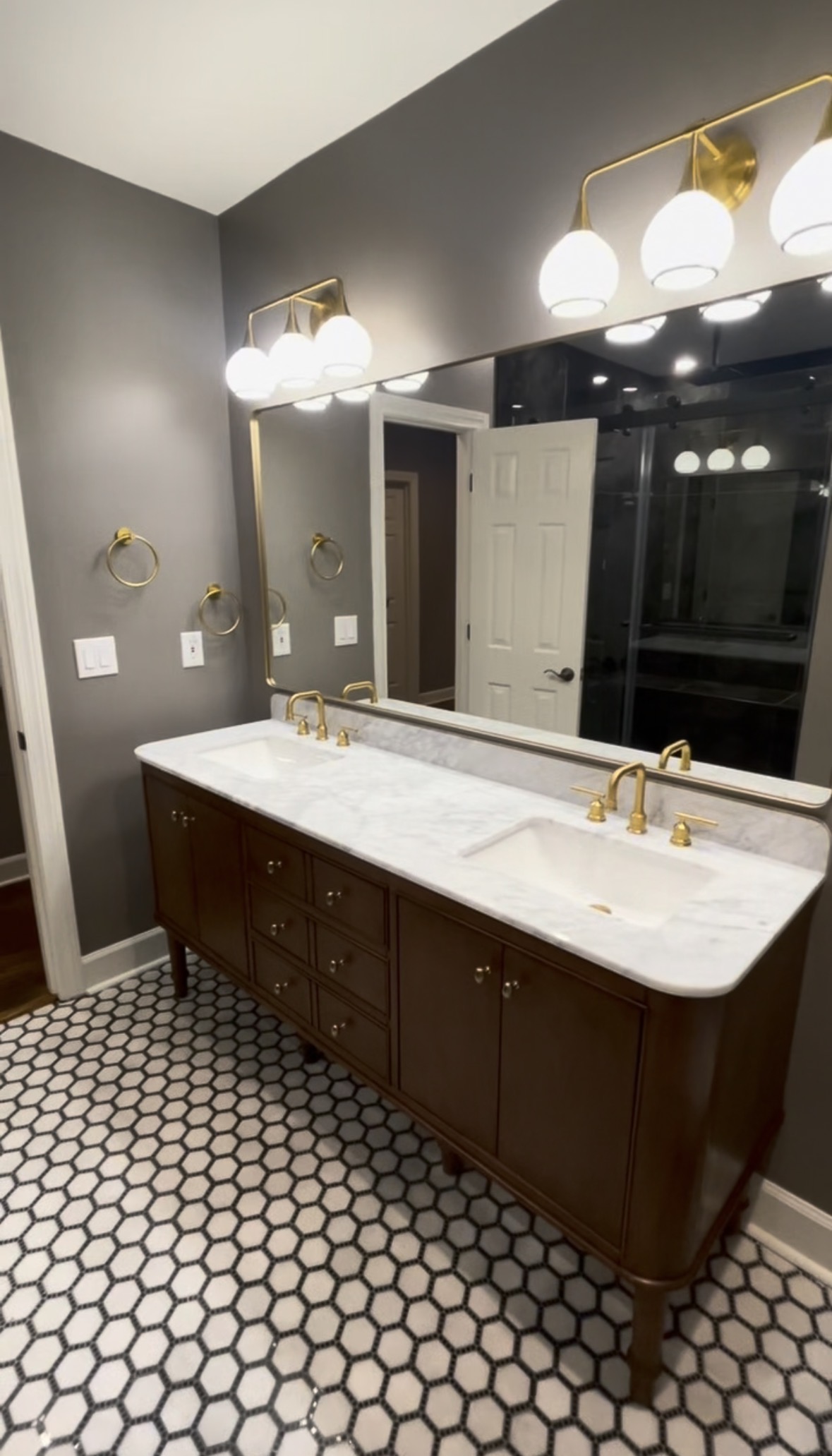Double vanity with marble top, brass fixtures and hex tile floor