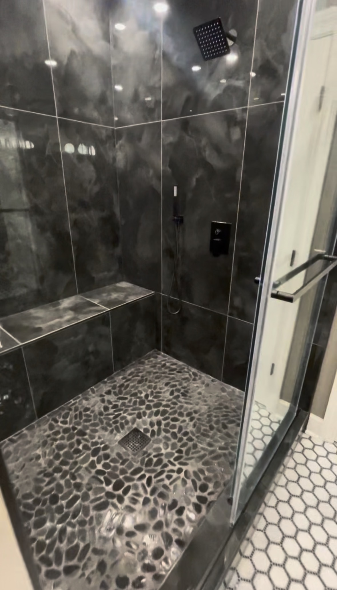 Walk-in shower with black tile, bench and pebble floor